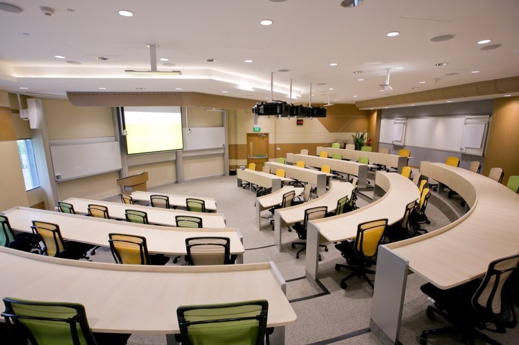 Lecture room at Assas University Singapore with curved tables, chairs, and a windowless interior designed for focused learning.