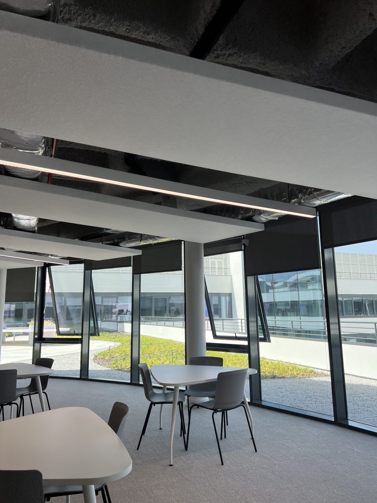 Lisbon campus library with a sleek concrete exterior and tall glass windows, surrounded by trees and open sky.