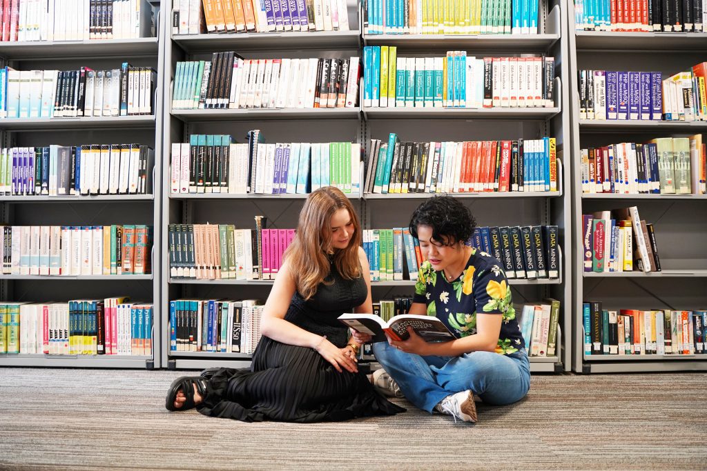 Two students reading a book on the library floor at James Cook University—capturing daily life while studying abroad in Singapore.