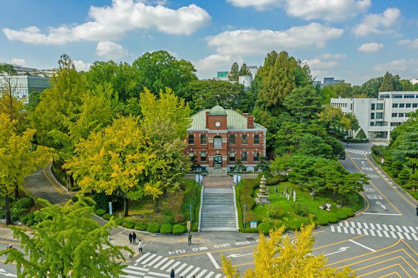 A charming red brick building with a clock tower surrounded by lush greenery on a university campus in Seoul, providing a serene and inspiring environment for those who want to study in Seoul.