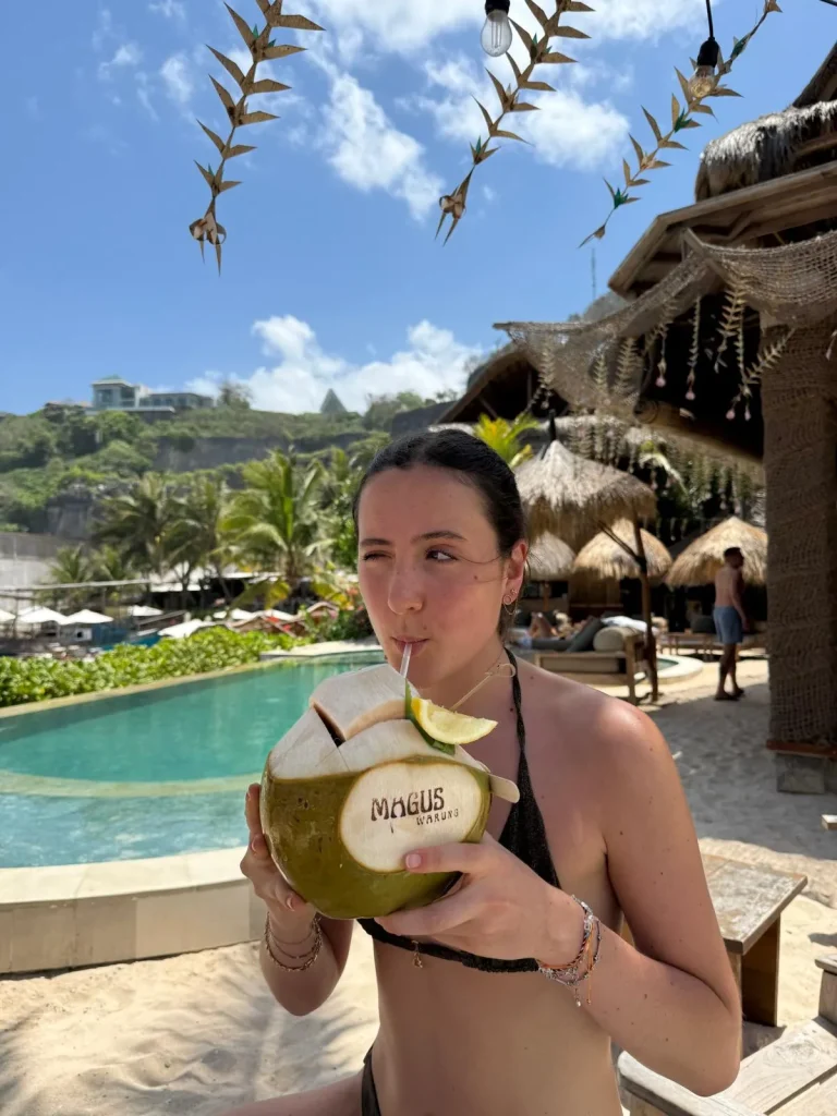 Emma, exchange student in Bali drinking from a coconut at the beach during her gap year